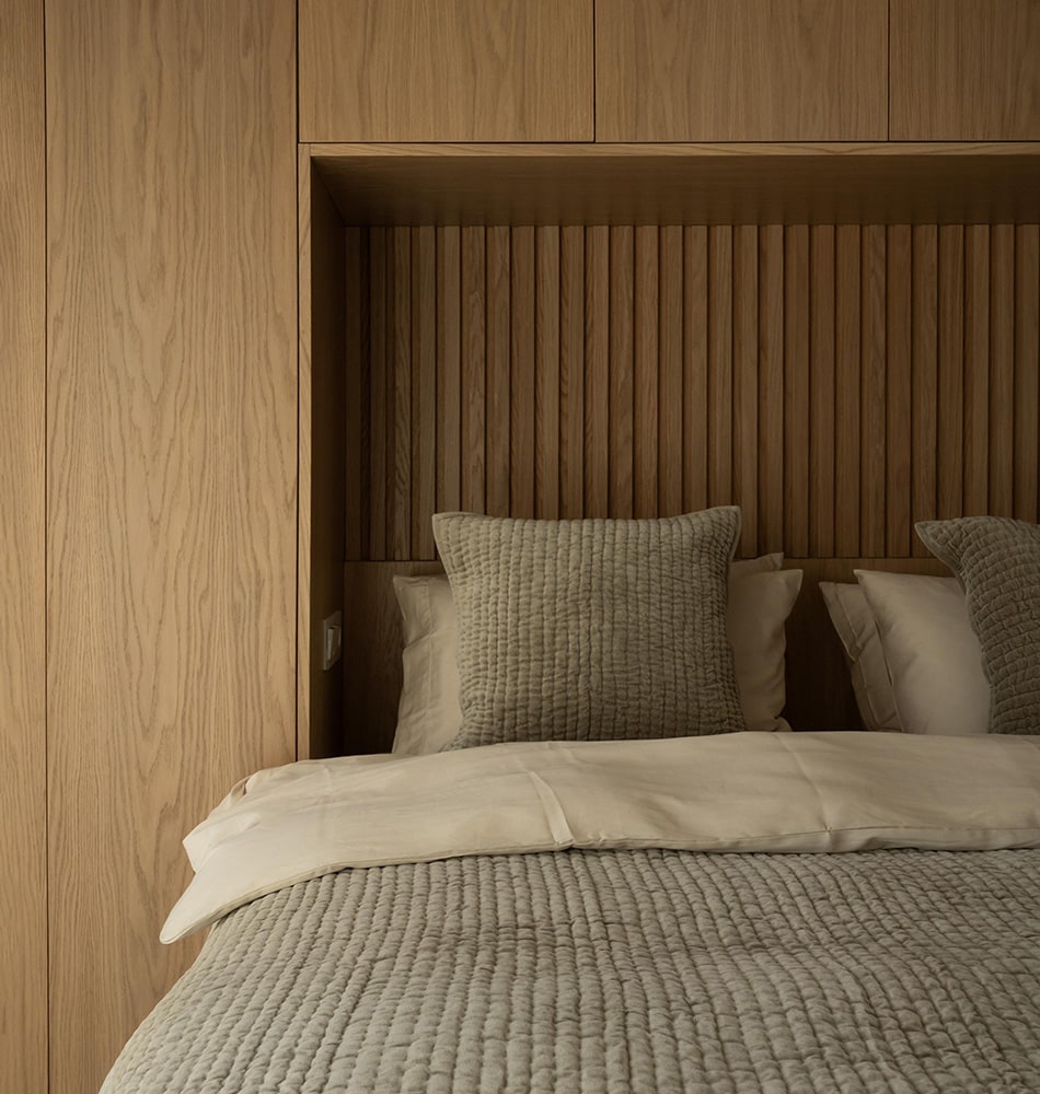 A close-up of a bed enveloped by warm wooden panels, complemented by lush green bedding, all in a newly renovated apartment.